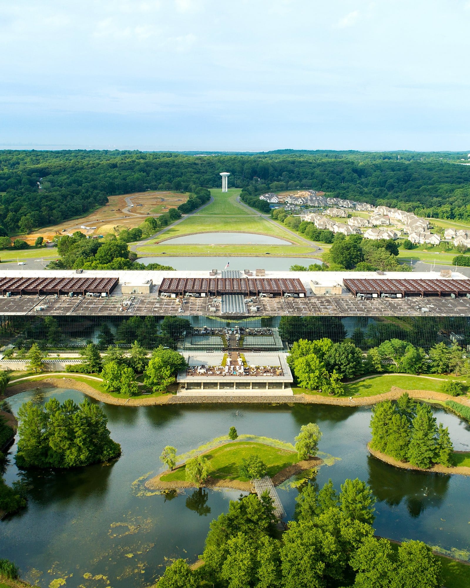 Aerial view of a vast modernist office campus with a long tree-lined allée and ponds